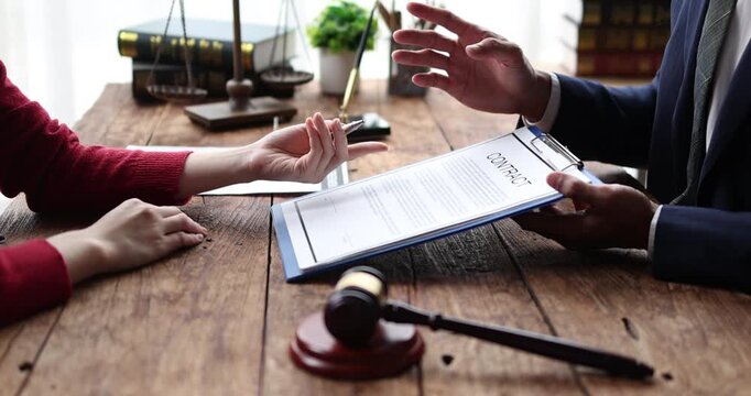 Lawyer and client discussing a contract agreement, financial paperwork, or legal document with a gavel and pen on a rustic wooden desk, offering legal advice