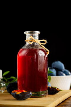 Sweet plum syrup with fresh plums on rustic wooden table