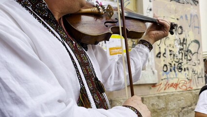 Adult man wearing a traditional embroidered vyshyvanka plays a vintage violin on city street. The scene emphasizes cultural identity, heritage and the expressive character of live music. Slow mo © ExpressVectors