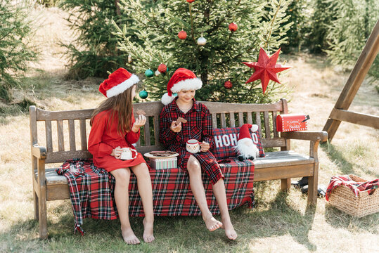 Christmas in July celebration with happy children wearing Santa hats, enjoying festive outdoor setting with Christmas decorations, gifts, evergreen trees and bright summer sunlight.