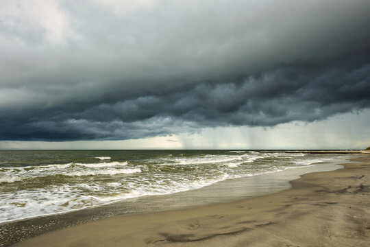 Storm clouds gather over the ocean as waves crash on the sandy beach in the early evening
