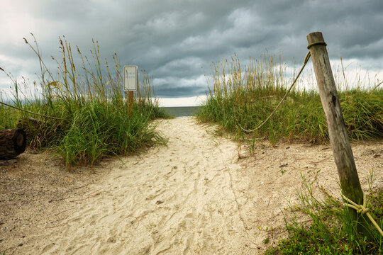 Path through grass leads to beach under cloudy sky