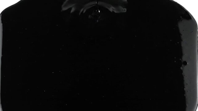 Thick black liquid pouring and spreading on white surface abstract viscous fluid motion and filling the frame