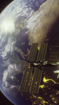 The image shows the International Space Station in orbit above Earth during the night. Cities are visible with lights shining on the surface. The coastlines and landforms are highlighted.