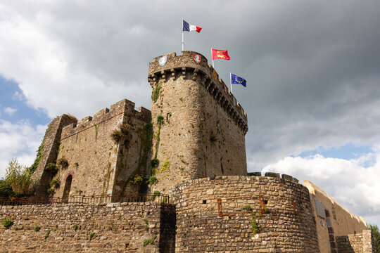 Stone keep and fortified wall of Chateau d Avranches with national and regional flags flying against a cloudy sky in Normandy France