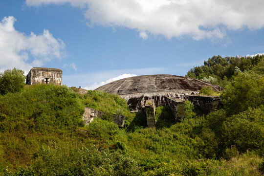 Massive concrete dome of La Coupole World War II bunker embedded in a grassy hillside under a partly cloudy blue sky in Saint Omer France