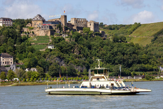 Passenger ferry cruising along the Rhine River past the medieval ruins of Burg Rheinfels on a forested hillside in Sankt Goar Germany