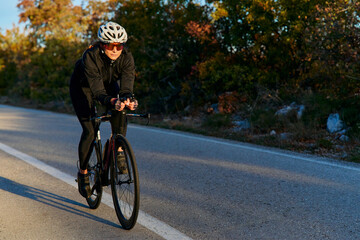 Naklejka premium Female Cyclist Training On Road Bike At Sunset During Autumn Outdoor Fitness Ride
