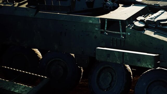 A large military vehicle moves over rough dirt ground during daylight. The scene shows the vehicles wheels and structure, highlighting its robust design and purpose.