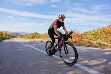 Fototapeta premium Female Cyclist Riding Road Bike Outdoors on Scenic Autumn Country Road for Fitness Training