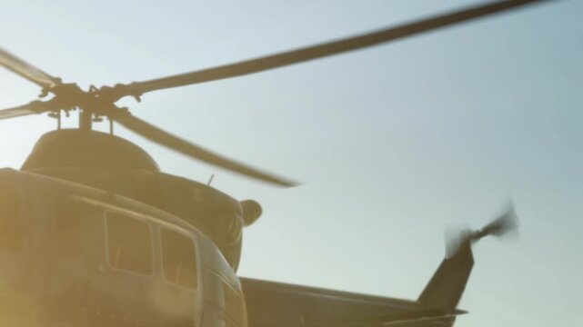 A helicopter prepares for takeoff in an open area. The sun shines brightly, highlighting the rotor blades. The scene captures the moment just before flight in a clear sky.