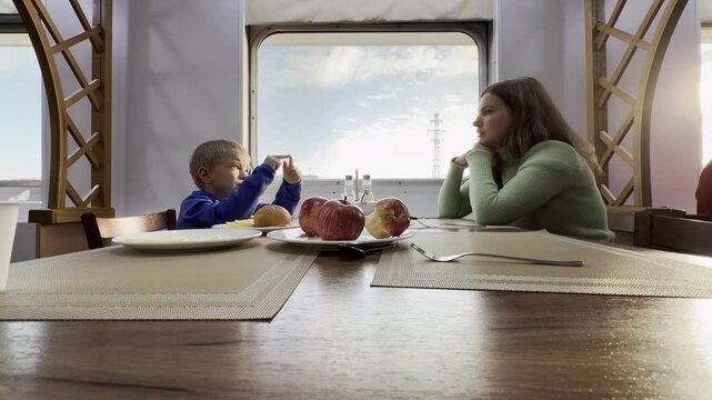 A mother and son sit and talk inside a cruise ship on the Neva River in Saint Petersburg. This cozy moment creates warm, happy, and peaceful feelings during their pleasant journey.