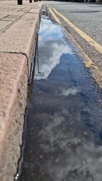Clouds reflected in a roadside puddle after rain in Cambridge England