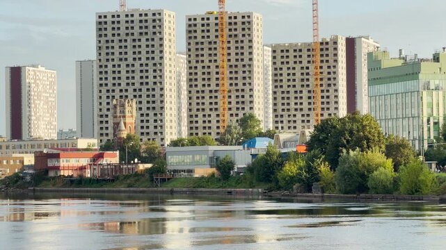 A modern building stands tall near the calm river. Construction cranes create a peaceful urban vibe. This lovely landscape features Saint Petersburg.