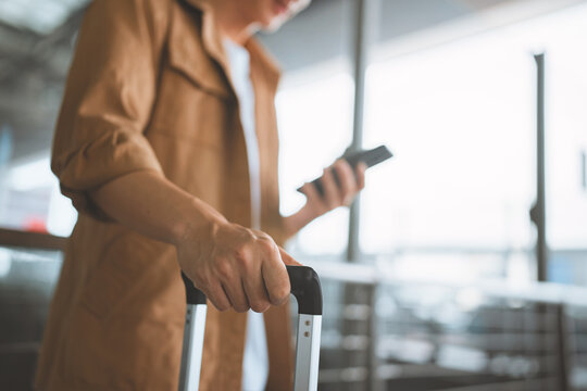 Traveler holding rolling suitcase and smartphone inside airport terminal, ready for departure, journey and vacation with mobile technology, transportation, luggage and contemporary travel lifestyle