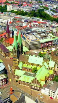 Vertical video. Bremen, Germany. St. Petri Dom zu Bremen, twin green copper spires and Romanesque-Gothic brick massing, aerial drone view orbiting the historic old town under bright summer sky. Drone