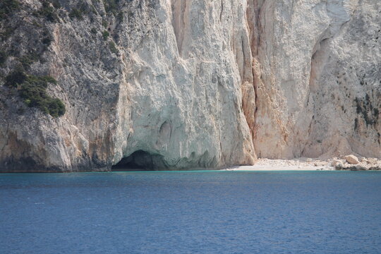 Sea cave under a high white limestone cliff. Beautiful Mediterranean seascape with deep blue water and hidden beach cove.