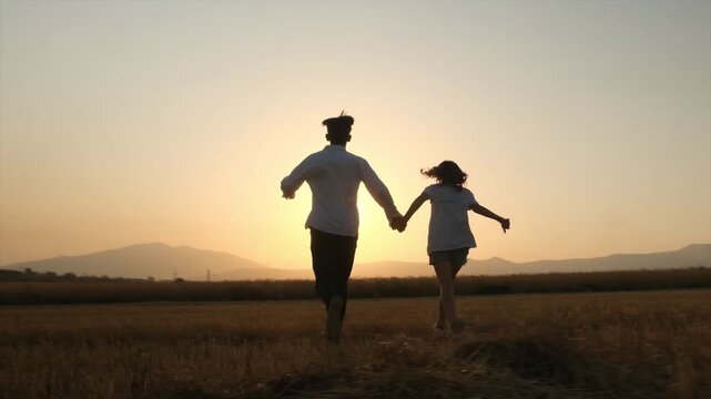 Camera follows young boy and girl running hand in hand at sunset, teenage romance and school love, happy relationship and togetherness, enjoying life outdoors, harvested field and mountain landscape