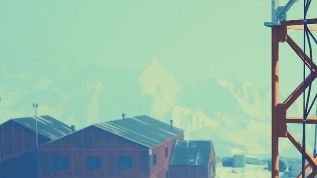 In a snowy area, red buildings sit close to mountains. A tall structure stands alongside. The sky is light and clear. This scene shows a cold, winter environment during the day.