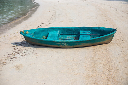 An empty green wooden boat sits on a sandy beach near the sea. Tropical island coast scenery, local fishing boat layout, summer holiday vacation.