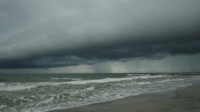 Dark clouds hang over a shoreline with waves breaking on a sandy beach during an approaching storm video