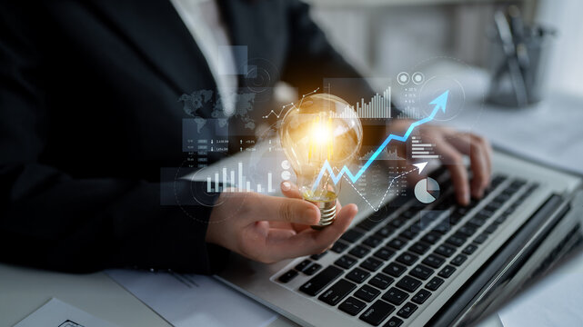A businessman holds a light bulb symbolizing innovation, while working on a laptop. Digital graphs illustrate growth and creativity in a modern office setting. Scalp