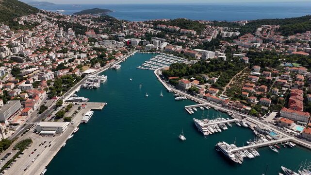 Aerial drone panorama of Gruz Harbor in Dubrovnik Croatia with turquoise water yachts boats and a dense coastal cityscape of red terracotta roofs and palms.