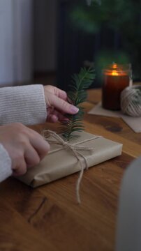 Hands inserting fresh green pine sprig under twine on rustic gift package, medium shot