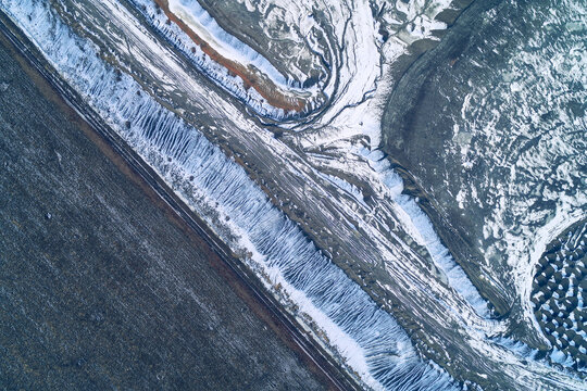 Diagonal pattern of snowy erosion gullies and icy ridges on slag heap surface, top view aerial shot