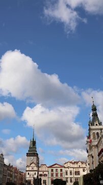 Vertical screen historic Pardubice Czechia town square sits beneath a bright blue sky with drifting white clouds elegant old architecture towers and colorful town facades