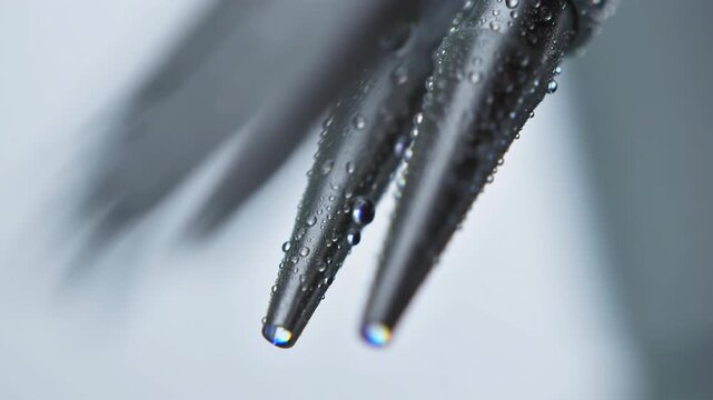 Wet metal prongs remain suspended in extreme close-up as tiny water droplets cling to their dark reflective surfaces against a soft pale background with shallow focus