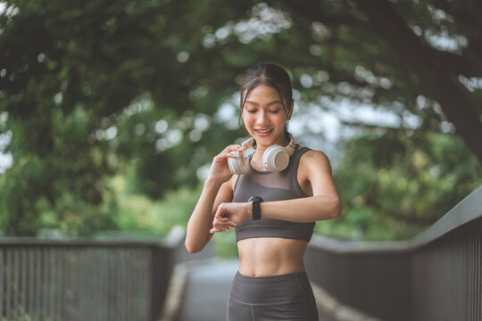 Sporty young woman checking smartwatch during outdoor workout with headphones around neck, fitness tracking, wearable technology, exercise, healthy lifestyle and active training in green park