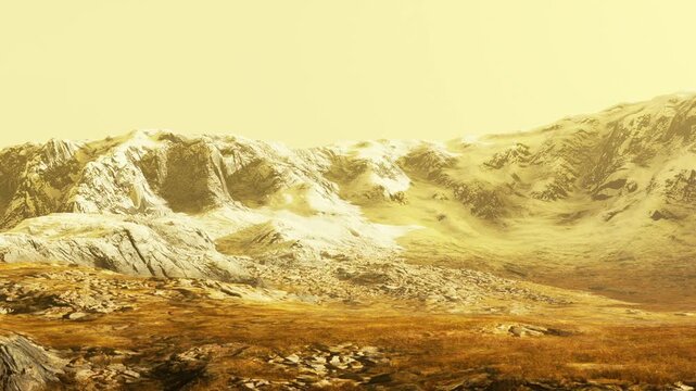 Mountains covered in snow rise against a yellow sky. The foreground has rocky ground with patches of grass. The setting appears remote and natural, showing rugged terrain.