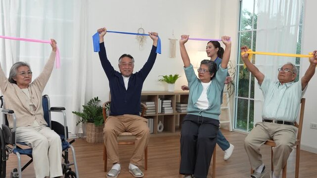An Asian nurse handed out ribbons containing exercise equipment to a group of elderly people, including some in wheelchairs, in a class at a nursing home