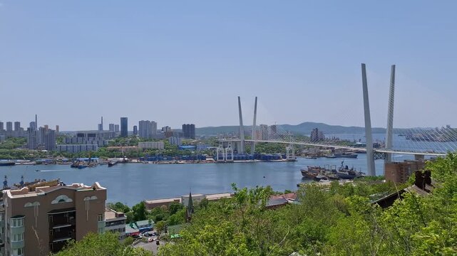 Majestic Zolotoy Rog bay cityscape spreads outdoors with the iconic Golden Bridge under a clear sky in Vladivostok, Russia. Coastal city skyline, maritime infrastructure landscape.