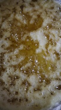Vertical screen homemade ghee cooks slowly as melted butter bubbles and foams during clarification separating milk solids to create pure golden clarified butter in kitchen