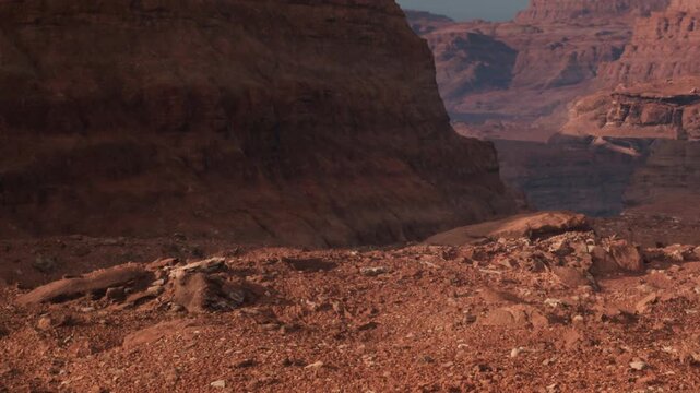 A rugged landscape with red rocks and cliffs in a desert area. The sunlight highlights the texture and shapes of the rocks. This landscape is part of the Grand Canyon.