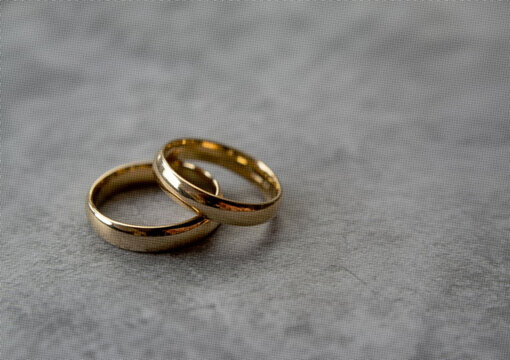 Two interlocking gold wedding rings resting on a textured grey stone surface close up view