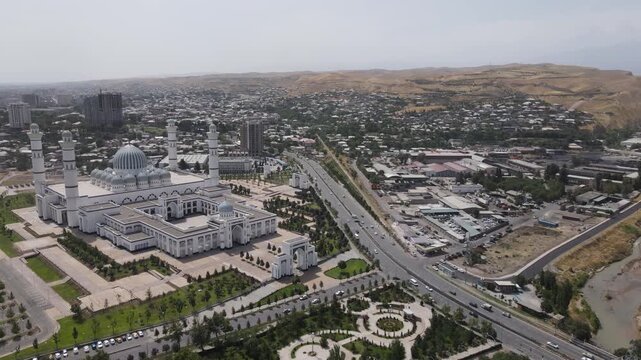 Aerial drone orbit around the Grand Mosque in Dushanbe, Tajikistan, with surrounding mountains, city roads and traffic on a sunny day
