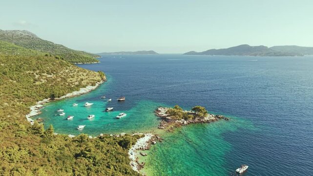 Aerial view of luxury yachts anchored in a turquoise bay surrounded by a rocky coastline and green forest. Summer seaside vacation scene. Drone view of the yachts.