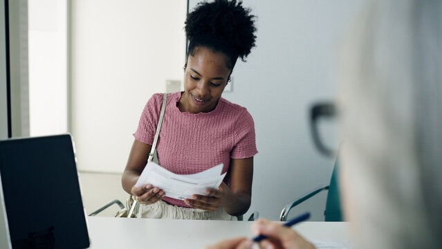 Patient submitting papers to a medical receptionist at a clinic, completing necessary forms for a healthcare appointment