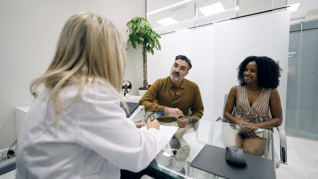 Female doctor having a medical consultation with a multi ethnic couple, discussing wellness and aesthetic healthcare options