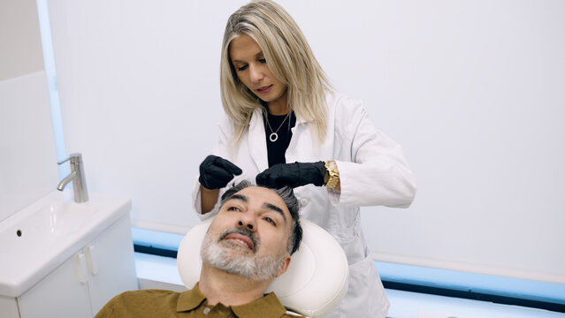 Female trichologist treating a male patient's scalp and hair loss in a medical clinic, focusing on hair regeneration procedures