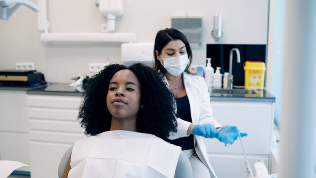 Dentist wearing protective face mask and gloves preparing tools for a dental check up with a patient in the clinic