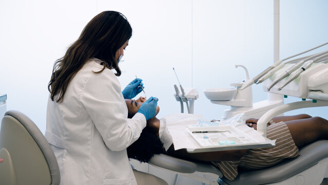 Dentist wearing gloves and mask examining a patient's teeth during a regular dental check up at a modern clinic