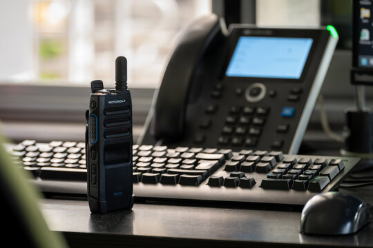 Motorola Solutions TLK 110 WAVE PTX radio positioned beside a computer keyboard and office telephone at a workplace workstation.