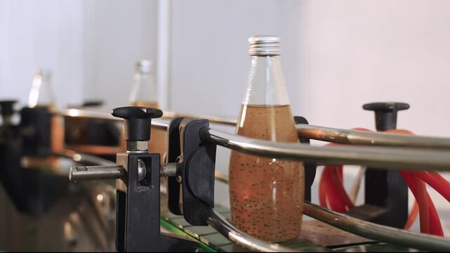 Juice in glass bottles on an automated conveyor belt in a modern beverage production facility line. Technology in the food and drink industry. Ready to drink fruit juice in a manufacturing factory. 