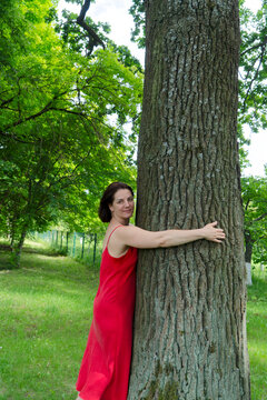 Person in red jacket caring outdoors. Enthusiastic volunteer with open arms in woodland setting. Dedicated individual in vibrant coat showing kindness amid sunlit forest trail