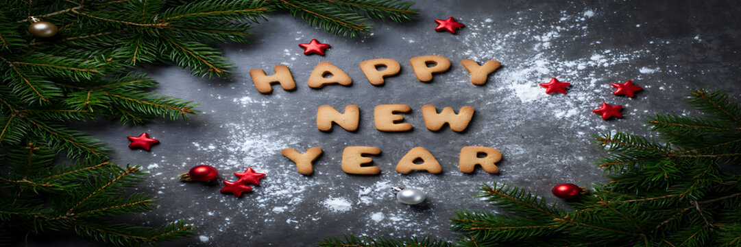 Festive holiday composition with gingerbread cookie letters spelling happy new year on a dark grey background, with pine branches, and ornaments