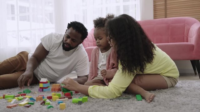 Family day concept. Happy African American father, mother, and child daughter sitting and playing with multicolored wooden blocks together with love and bonding on the floor in the living room at home